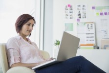 Woman sitting on a couch looking at a laptop.