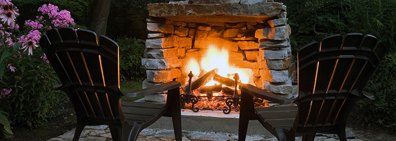 Decorative image showing 2 patio chairs in front of a cozy outdoor fireplace.